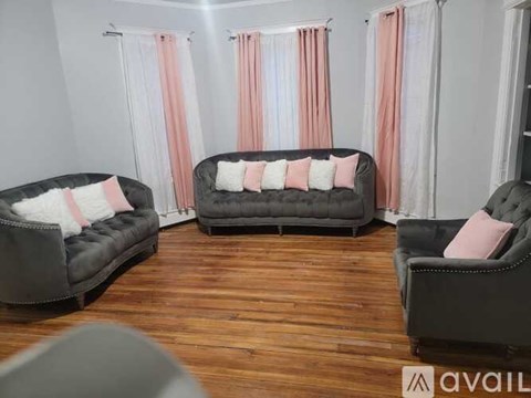 A living room with a grey couch and a black couch with pink pillows.