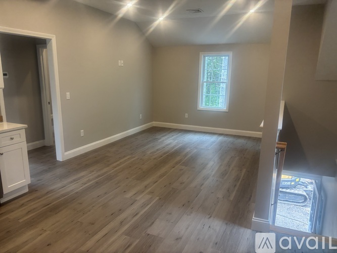 A room with wooden flooring and a window with a view of trees.