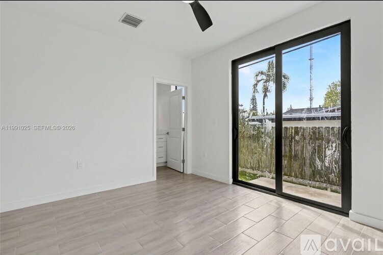 A room with a sliding glass door leading to a balcony with a view of a building and trees.