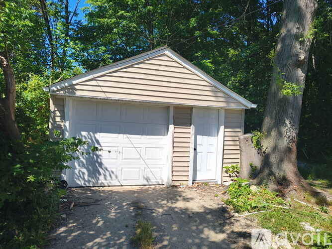 A small garage with a white door is surrounded by trees.