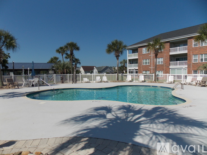 A pool surrounded by a white fence and palm trees.