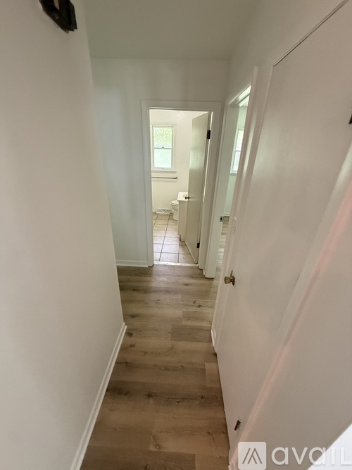 A hallway with white walls and wooden floors leading to a door.
