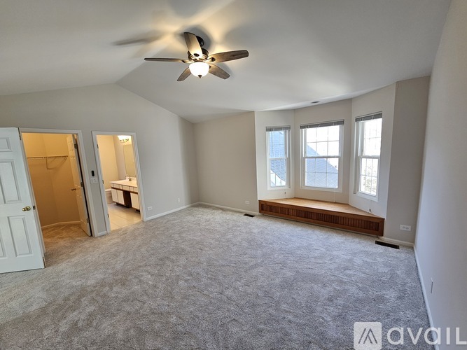 A room with a carpeted floor, a ceiling fan, and a window with a view of a building outside.