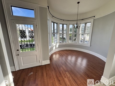 A room with a white door and a window with a view of a fence and a building.