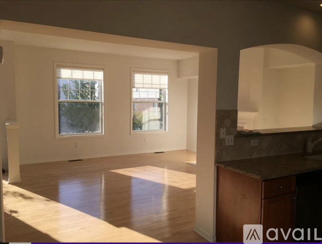 A spacious room with wooden floors and two windows letting in natural light.