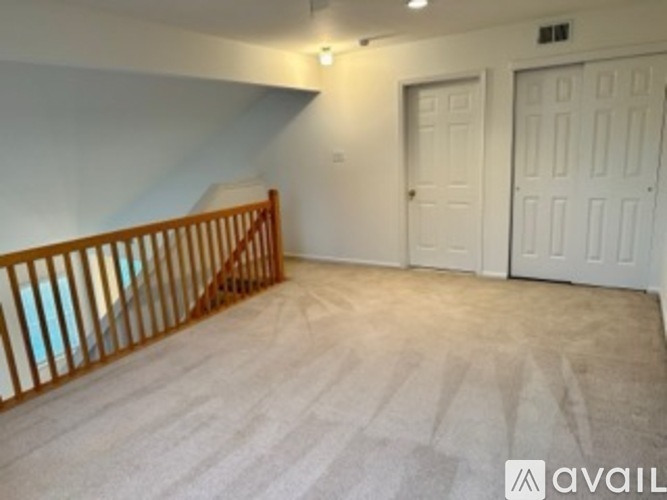 A room with a carpeted floor, a staircase with wooden railings, and two doors.
