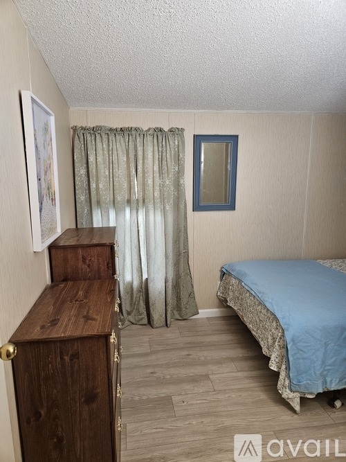 A bedroom with a bed, dresser, and window with curtains.