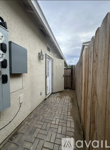 A narrow alley with a wooden fence on one side and a building with a grey electrical box on the other.