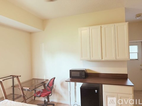 A kitchen area with a microwave, a chair, and a trash bin.