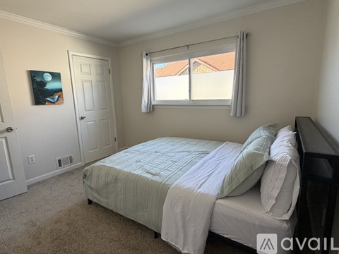 A bedroom with a bed, window, and a painting on the wall.
