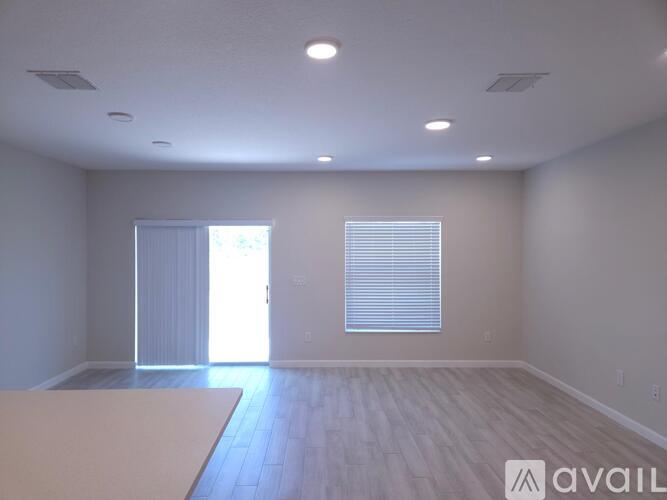 A spacious room with wooden flooring and a large window with blinds.