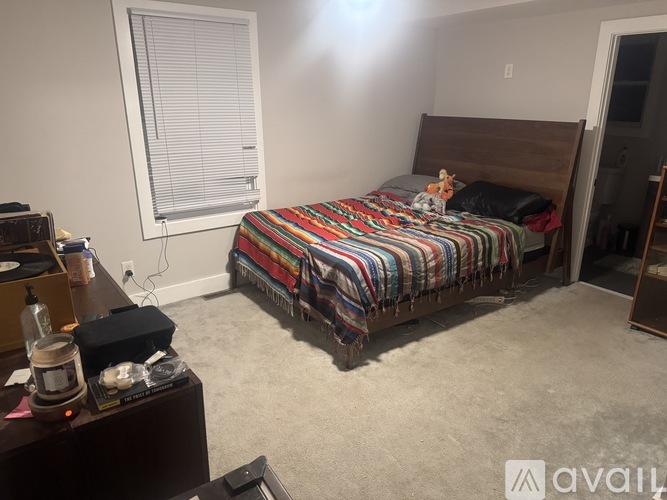 A bedroom with a bed, nightstand, and window with blinds.