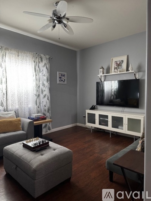 A living room with a grey couch, a grey ottoman, a white TV stand, and a ceiling fan.