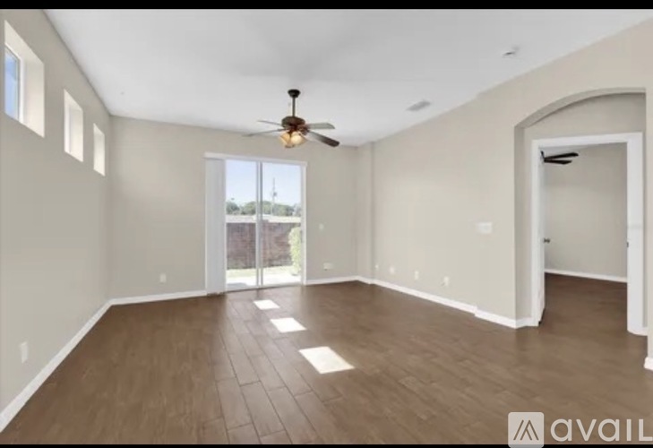 A spacious room with a ceiling fan and sliding glass doors leading to a balcony.