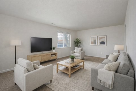 A living room with a grey couch, a white armchair, a wooden coffee table, and a flat-screen TV.
