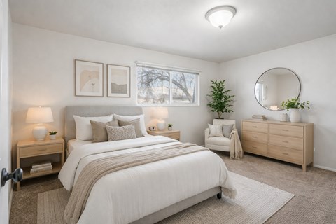 A bedroom with a large bed, a nightstand with a lamp, a chair, and a round mirror on the wall.