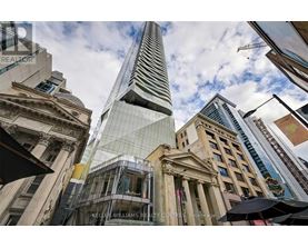 A tall building with a glass facade stands in front of a row of older buildings.