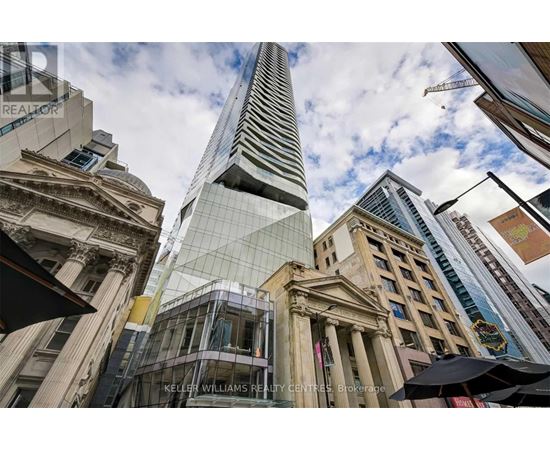A tall building with a glass facade stands in front of a row of older buildings.