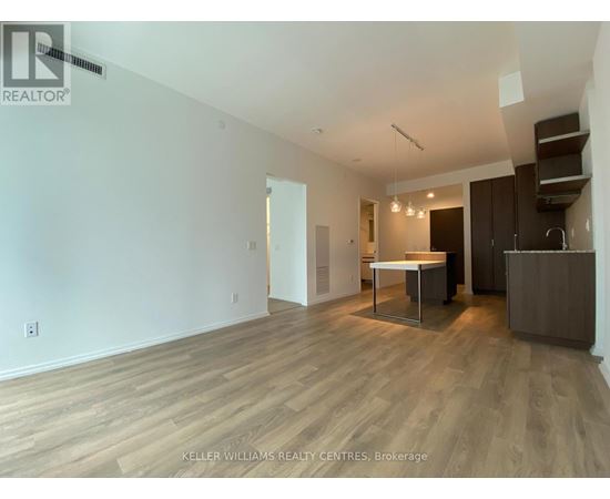 A spacious room with wooden flooring and a kitchen area with a table and chairs.