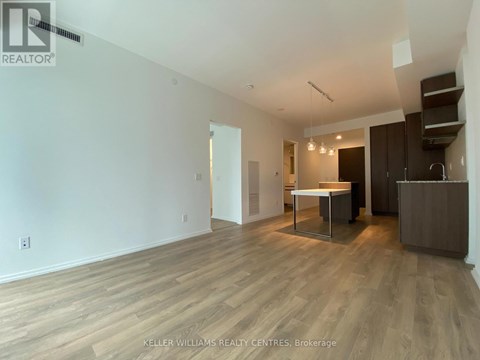 A spacious room with wooden flooring and a kitchen area with a table and chairs.