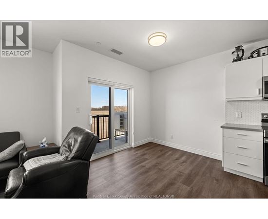 A living room with a black leather chair and a kitchen area with white cabinets.
