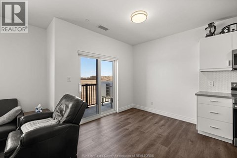 A living room with a black leather chair and a kitchen area with white cabinets.