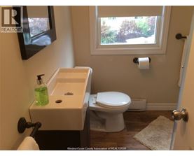 A white toilet is in a bathroom with a sink and a window.