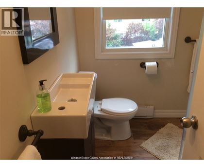A white toilet is in a bathroom with a sink and a window.