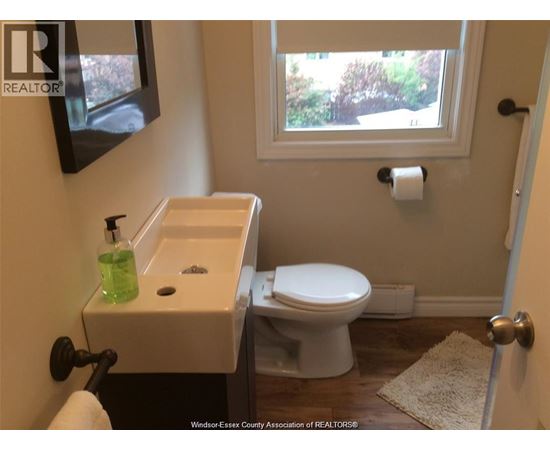 A white toilet is in a bathroom with a sink and a window.