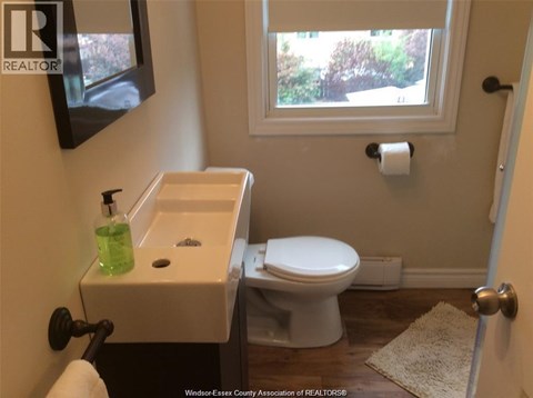 A white toilet is in a bathroom with a sink and a window.