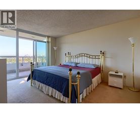 A bedroom with a large bed and a balcony with a view of the city.