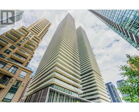 A tall building with a glass facade stands in front of other buildings.