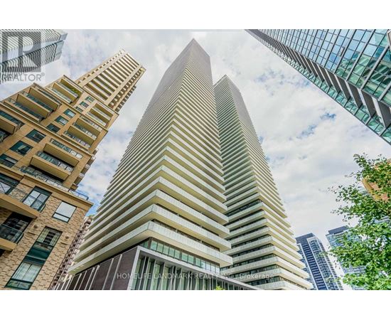 A tall building with a glass facade stands in front of other buildings.