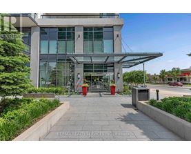 The image shows the front of a modern building with a glass facade and a covered walkway leading to the entrance.