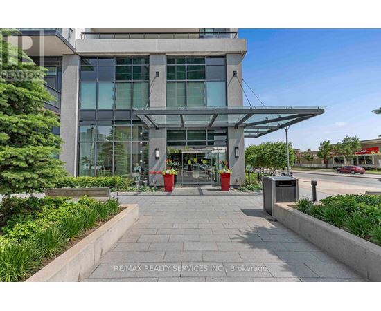 The image shows the front of a modern building with a glass facade and a covered walkway leading to the entrance.