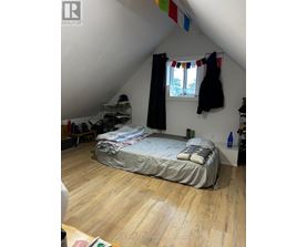 A bedroom with a bed, a window with curtains, and a coat hanging on the wall.