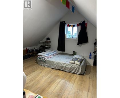 A bedroom with a bed, a window with curtains, and a coat hanging on the wall.