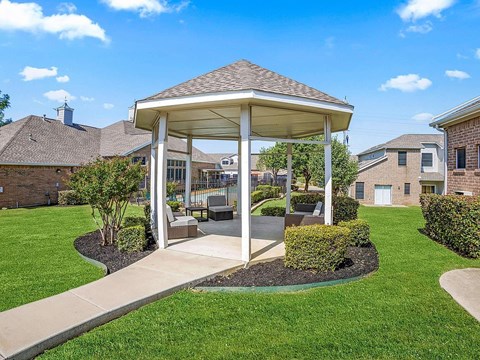 A gazebo is surrounded by a grassy area and a concrete walkway.