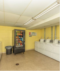 A yellow wall with a vending machine and a trash can.