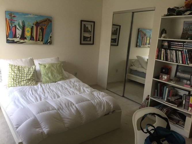 A bedroom with a white bed and a bookshelf filled with books.