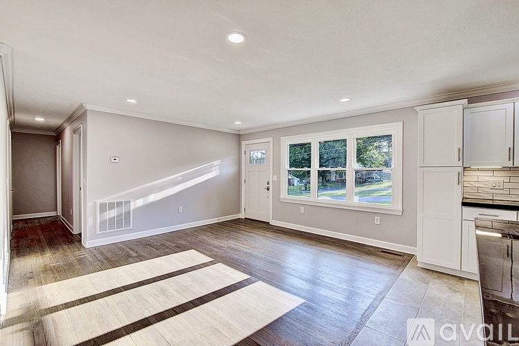 A spacious living room with a large rug and a kitchen area in the background.