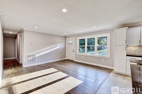 A spacious living room with a large rug and a kitchen area in the background.