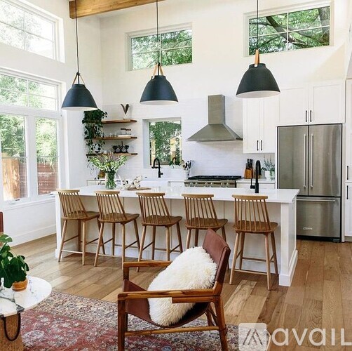 A kitchen with white cabinets and a white island with a bar stool in front of it.