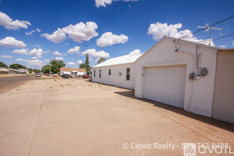 A white building with a garage door is in the foreground of a sunny day.