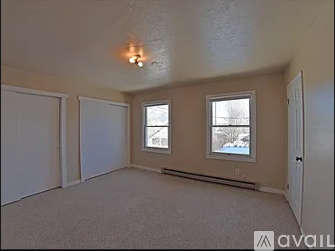 A room with a carpeted floor, two windows, and a door.