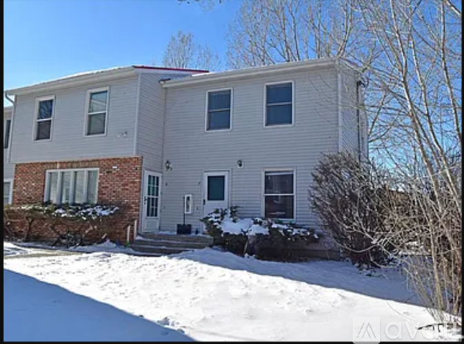 A house with a grey siding and a brick foundation is surrounded by snow.