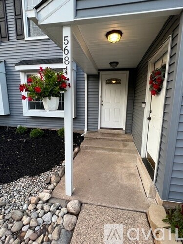 A grey house with a white door and a window with red flowers.