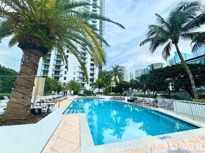 A pool surrounded by palm trees and a white fence.