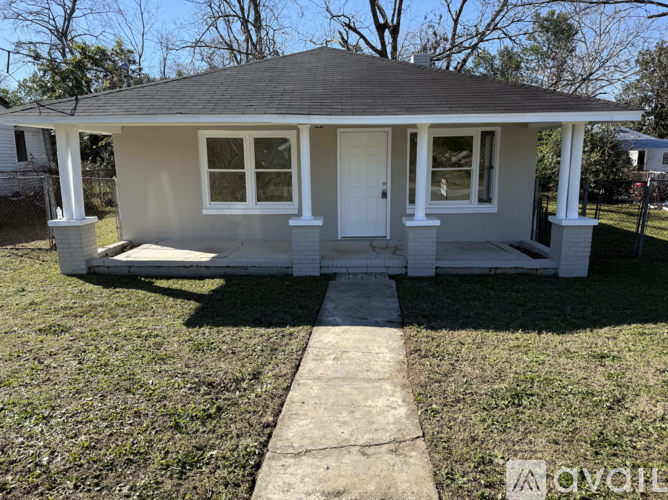 A small house with a white door and windows is surrounded by a grassy area.