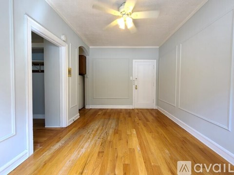 A room with wooden floors and white walls, with a ceiling fan and a door on the right.